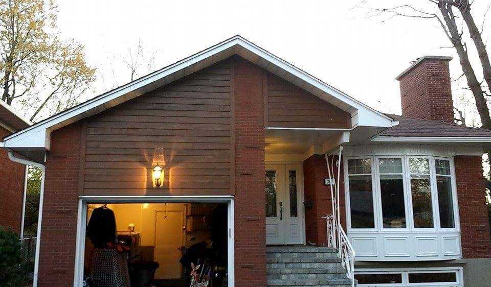Close-up of a house corner with brown lap siding on the gable and brick veneer below, white eavestrough along the roofline, and an open garage door