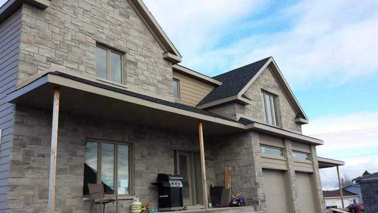 Large stone-clad two-storey home with covered porch and double garage — Gouttières et Revêtements Synergy