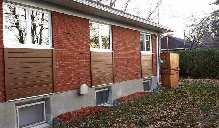 Brick home with wood-look composite skirting along the foundation — Gouttières et Revêtements Synergy