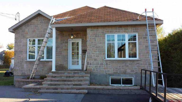 Deux échelles appuyées sur le toit d'une maison de pierre lors de travaux de gouttières