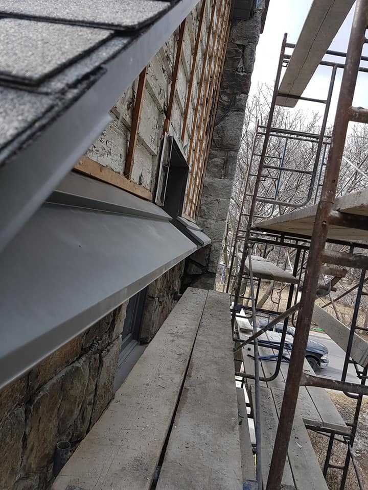 New gutter and fascia installation in progress on a stone-clad wall, scaffolding visible — Gouttières et Revêtements Synergy