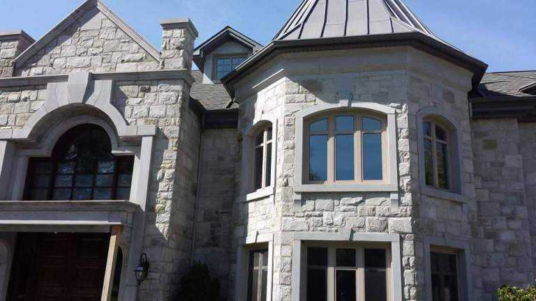 Close-up of a stone-clad house corner with a round turret featuring an arched window and a peaked metal roof