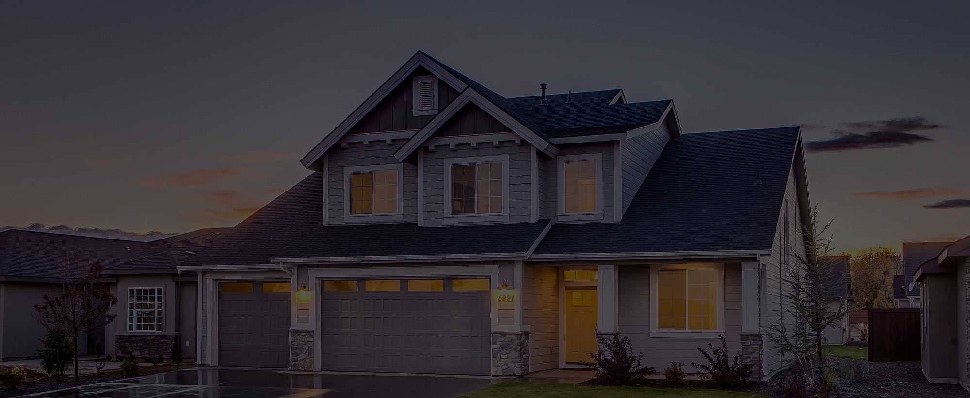 Suburban two-storey home at dusk with illuminated garage and entrance — Gouttières et Revêtements Synergy