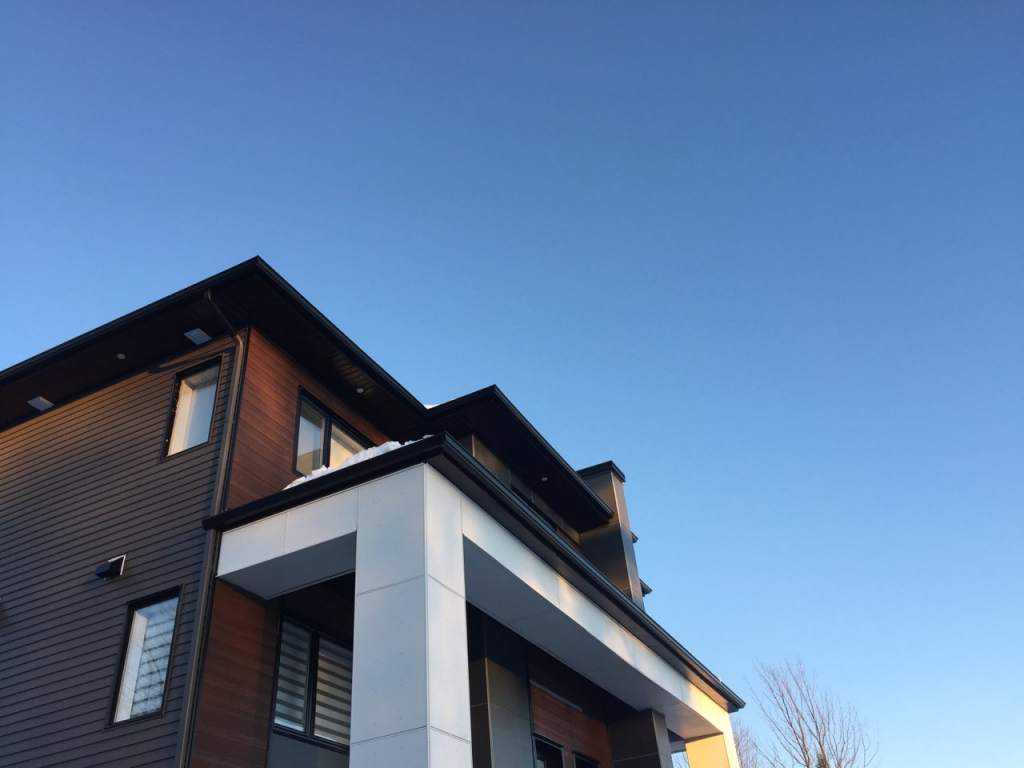 Maison moderne : déclin gris et déclin bois, panneaux clairs, soffites et fascias noirs — Gouttières et Revêtements Synergy