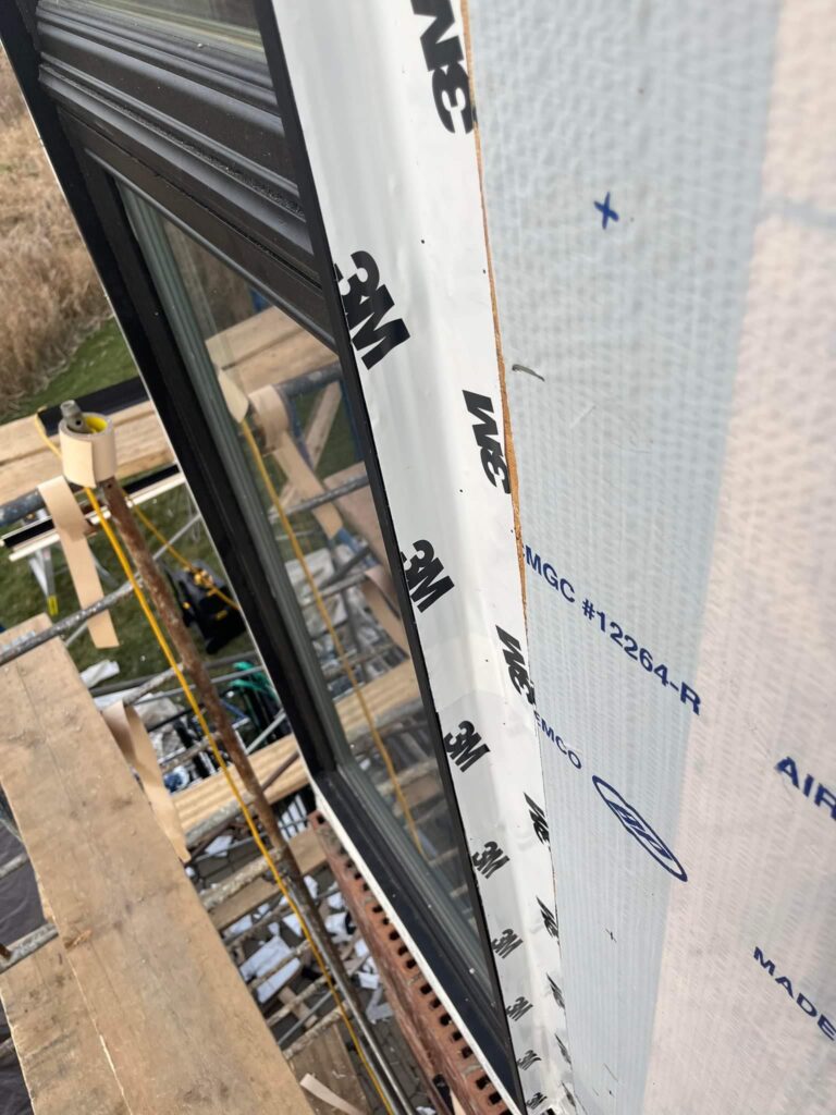 Cadre de fenêtre foncé, pièce blanche sous film protecteur et membrane pare-air; échafaudage en contrebas