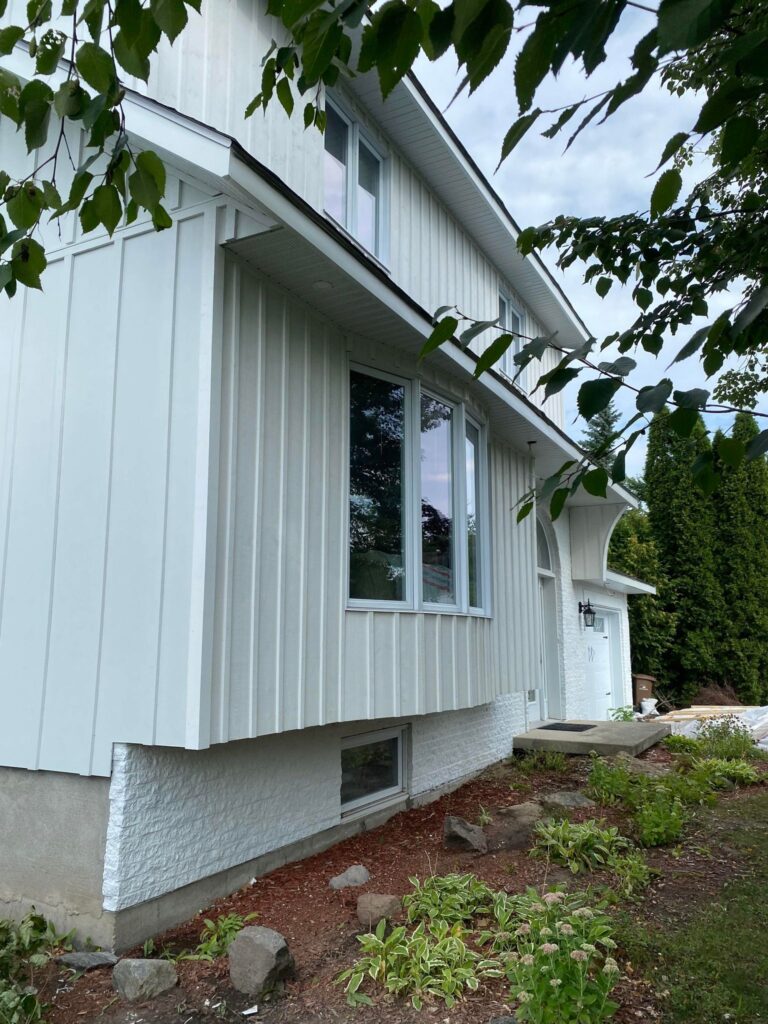 Maison au revêtement vertical blanc, soffite et fascia blancs, gouttière au toit — Gouttières et Revêtements Synergy