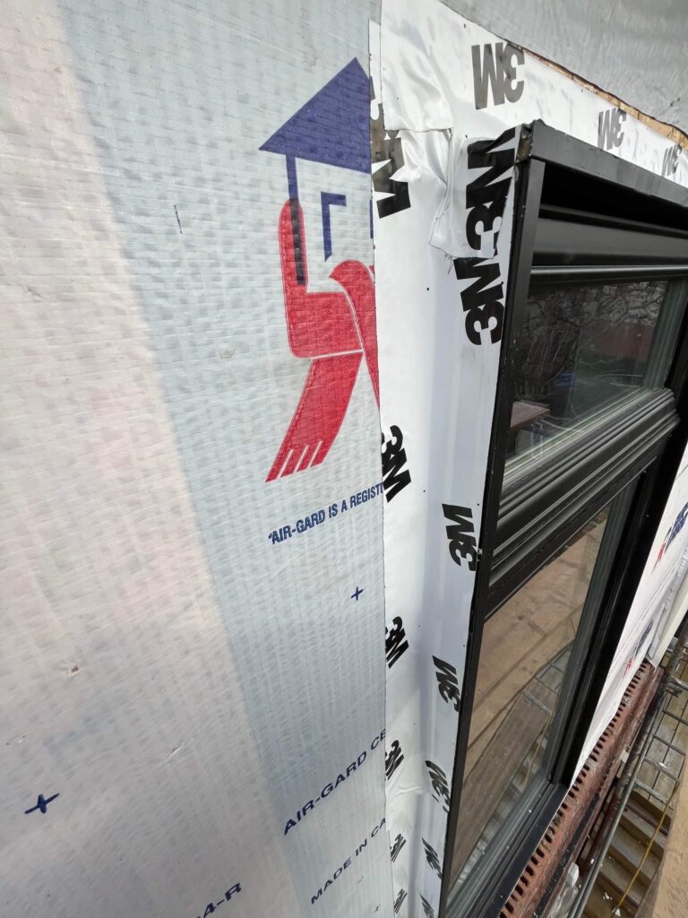 Gros plan en angle d'un mur recouvert d'une membrane pare-air blanche, près d'un cadre de fenêtre noir