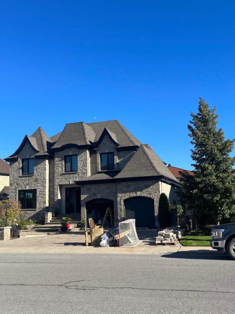 Maison en pierre à toiture grise, gouttières noires aux avant-toits et descente — Gouttières et Revêtements Synergy