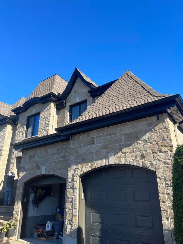 Gouttières noires et fascia sur avant-toits d'une maison en pierre à toiture de bardeaux — Gouttières et Revêtements Synergy