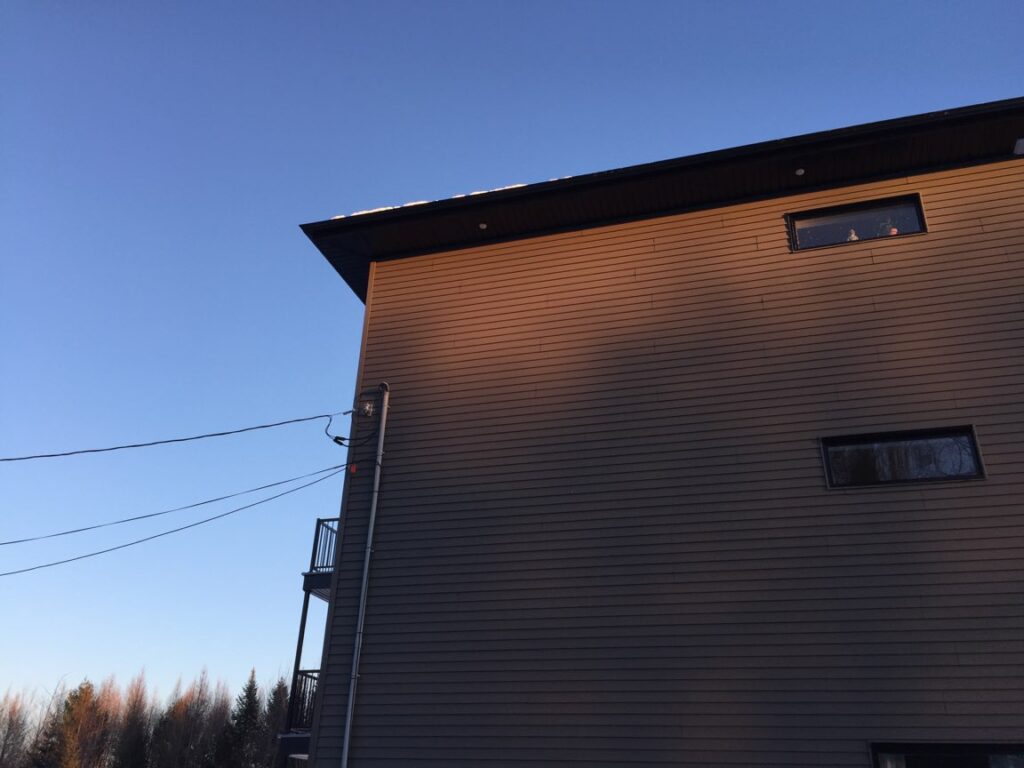 Mur en déclin horizontal gris-brun avec soffite et fascia foncés au débord de toit — Gouttières et Revêtements Synergy
