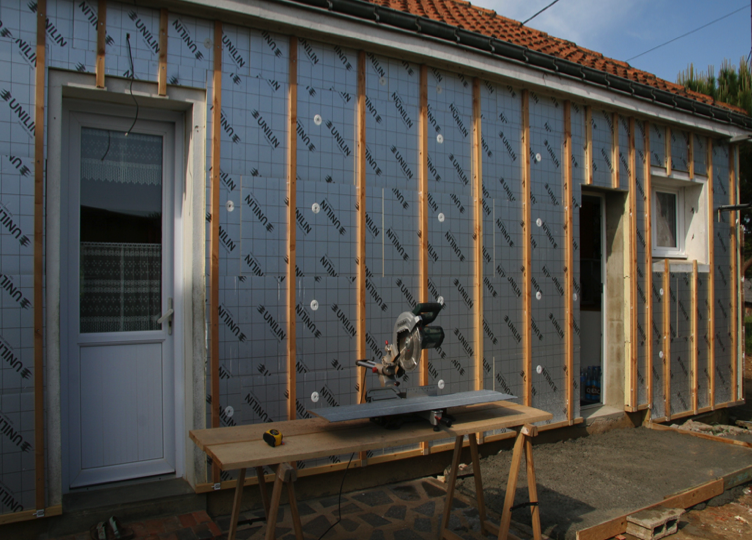 Installation de panneaux isolants rigides sur ossature de bois en rénovation extérieure, avec scie à onglet sur table de travail — Gouttières et Revêtements Synergy