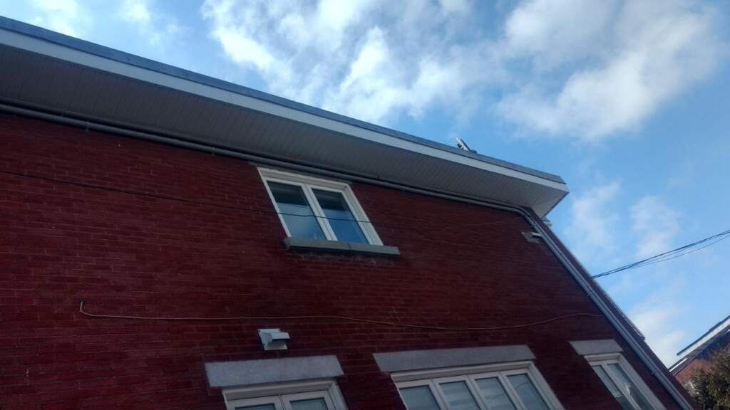 Débord de toit en contre-plongée : soffite ventilé et fascia clairs sur brique rouge — Gouttières et Revêtements Synergy